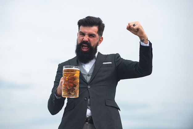 Glücklicher eleganter Mann, der Bier trinkt. Aufgeregter Brauer, der Glas mit Bier hält Ausdruck von Emotionen.