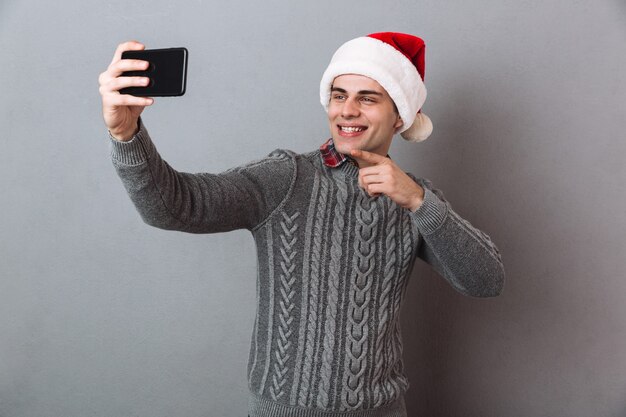 Glücklicher emotionaler Mann, der Weihnachtshut trägt, machen Selfie per Telefon.