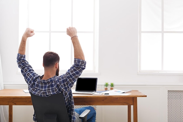 Glücklicher erfolgreicher Geschäftsmann gewinnen, im Büro feiern, am Arbeitsplatz sitzen, Rückseite. Kopieren Sie Platz auf dem Bildschirm.