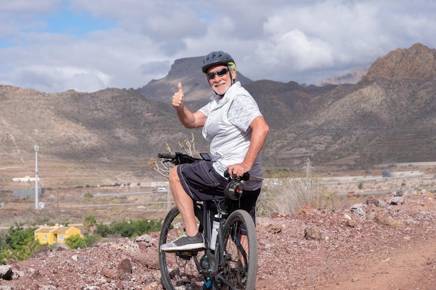 Glücklicher erwachsener aktiver älterer Mann, der mit seinem Fahrrad auf einer Landstraße fährt und einen gesunden Lebensstil genießt