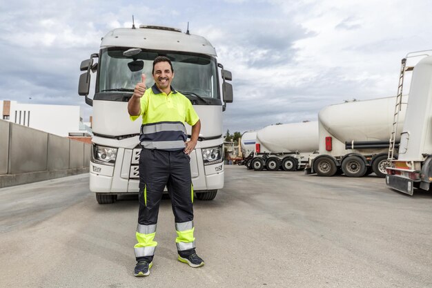 Glücklicher erwachsener Mechaniker, der mit erhobenem Daumen vor einem geparkten LKW im Servicecenter steht