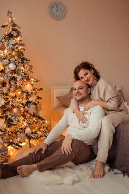 Glücklicher Familienmann und Ehefrau umarmen sich zu Hause auf dem Bett in der Nähe des Weihnachtsbaumes.