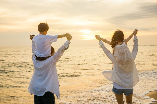 Glücklicher Familientag. Eltern, die bei Sonnenuntergang Kinder auf den Schultern am Strand tragen, Vater, Mutter und Kinder spielen zusammen im Freien am Sommerstrand, Familie im Urlaub, Sommerferienreise