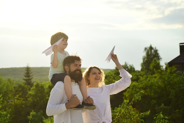 Glücklicher Familienvater, Mutter und Kind auf der Wiese mit einem Spielzeugpapierflugzeug im Sommer auf dem Naturhintergrund Gartenparty in Amerika Eltern und Kind
