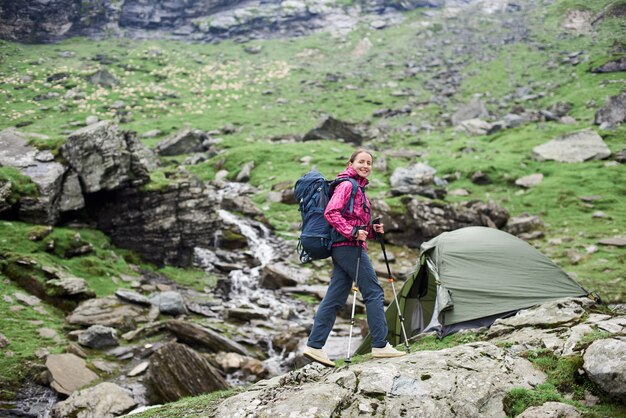 Glücklicher Frauenwanderer, der zur Kamera lächelt, die in den Bergen Tal geht