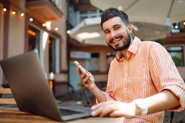 Glücklicher freiberuflicher Mann lächelt, während er am Laptop mit Telefon arbeitet Online-Konferenz Blog-Konzept