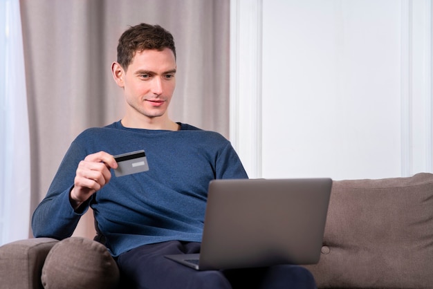 Glücklicher fröhlicher junger Mann, gutaussehender Mann mit Kreditkarte, die online im Geschäft zahlt, Informationen eingibt, einkauft