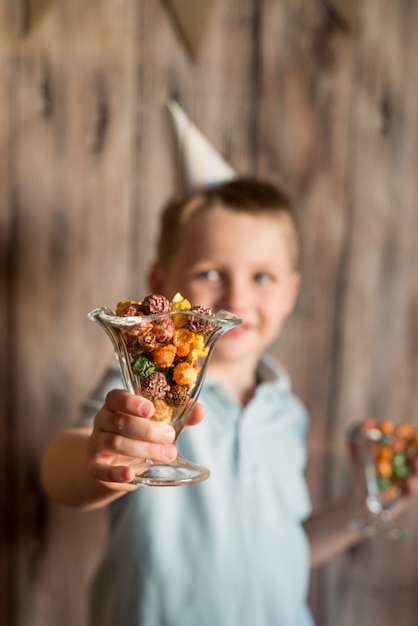 Glücklicher froher lachender kleiner Junge an einer Party. Hält ein buntes Popcorn in einem Glas.