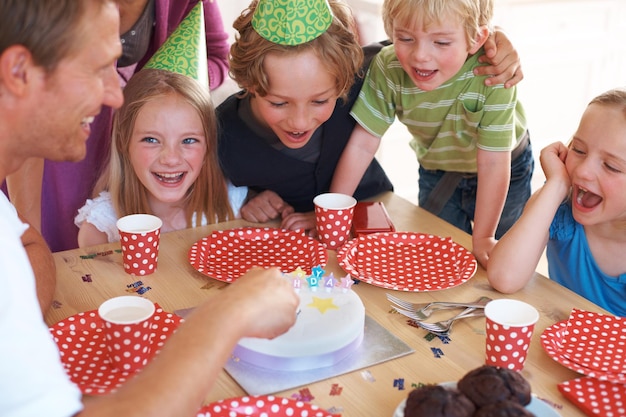 Foto glücklicher geburtstagskuchen dekoration und feier durch tischfeier und spaß zu hause mit wellness vater kinder und aufgeregte familie durch muffins kerzen und hüte mit liebe für ein besonderes ereignis im haus