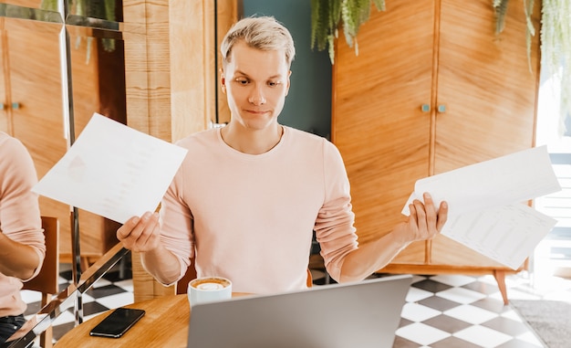 Glücklicher Geschäftsmann, der an der Cafeteria mit Laptop und Dokumenten sitzt. Geschäftsmann, der in einem Café sitzt, arbeitet und E-Mail auf Computer überprüft