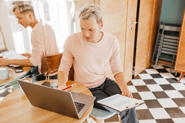 Glücklicher Geschäftsmann, der an der Cafeteria mit Laptop und Dokumenten sitzt. Geschäftsmann, der in einem Café sitzt, arbeitet und Zeitplan überprüft