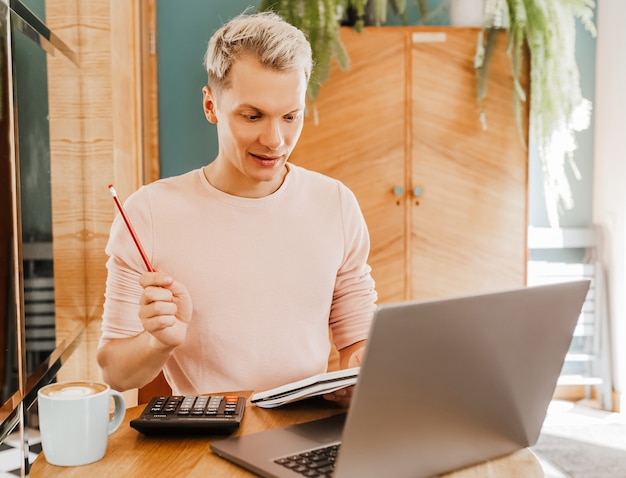 Glücklicher Geschäftsmann, der an der Cafeteria mit Laptop und Smartphone sitzt. Geschäftsmann, der auf Smartphone schreibt, während er in einem Café sitzt, arbeitet und E-Mail auf Computer überprüft