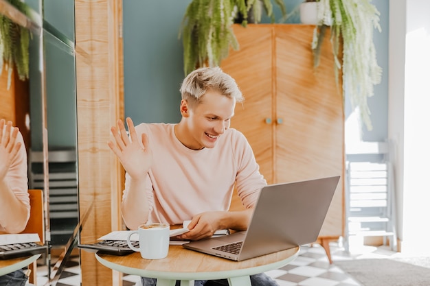 Glücklicher Geschäftsmann, der an der Cafeteria mit Laptop und Smartphone sitzt. Geschäftsmann, der auf Smartphone schreibt, während er in einem Café sitzt, arbeitet und E-Mail auf Computer überprüft