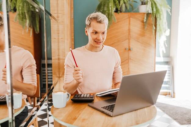 Glücklicher Geschäftsmann, der an der Cafeteria mit Laptop und Smartphone sitzt. Geschäftsmann, der auf Smartphone schreibt, während er in einem Café sitzt, arbeitet und E-Mail auf Computer überprüft