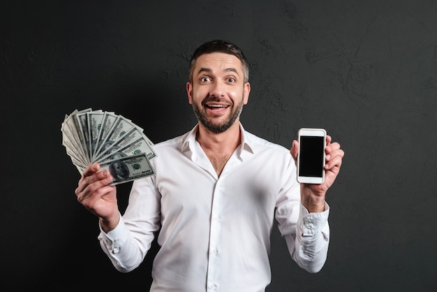 Glücklicher Geschäftsmann, der Anzeige des Handys zeigt, der Geld hält.