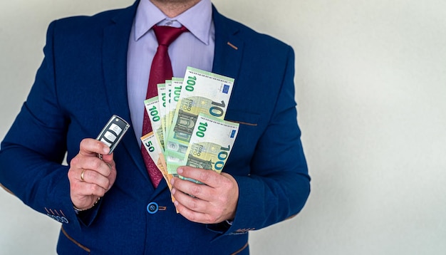 Glücklicher Geschäftsmann, der Autoschlüssel mit Eurogeld im Büro hält. Finanzierungskonzept