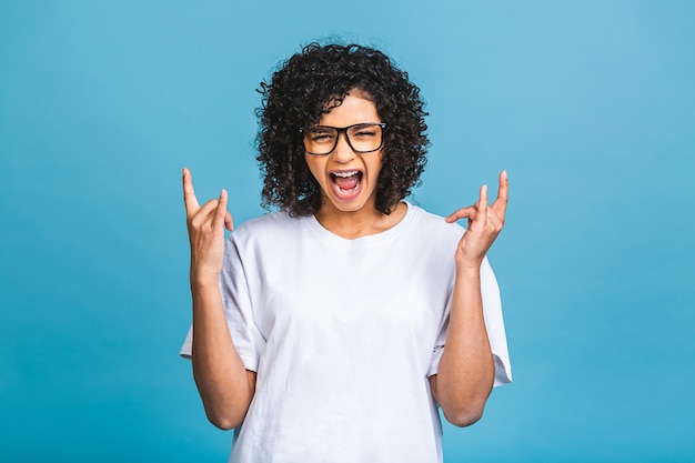 Glücklicher Gewinner! Foto der fröhlichen schönen jungen Afroamerikanerfrau, die lokal über blauem Wandhintergrund steht. Schauende Kamera, die Siegergeste zeigt.