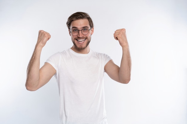 Glücklicher Gewinner. Glücklicher junger gutaussehender Mann, der beim Stehen vor weißem Hintergrund gestikuliert und den Mund offen hält.