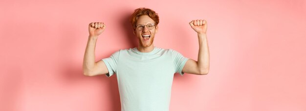 Glücklicher Gewinner mit roten Haaren und Bart, der den Sieg feiert, vor Freude „Ja“ ruft und die Hände hebt