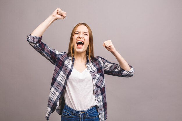 Glücklicher Gewinner! Nahaufnahme der emotionalen jungen attraktiven Frau mit Händchenhalten in den Fäusten, lokalisiert auf grauer Wand. Überraschte junge Frau schreit.