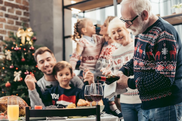 glücklicher großvater, der zu weihnachten wein in gläser für seine familie gießt