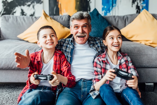 Glücklicher Großvater und Kinder, die Videospiel spielen, während sie zu Hause auf dem Boden liegen.