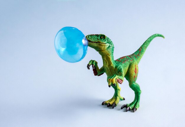 Glücklicher grüner Spielzeugdinosaurier mit blauer Kaugummi-Blase auf blauem Hintergrund