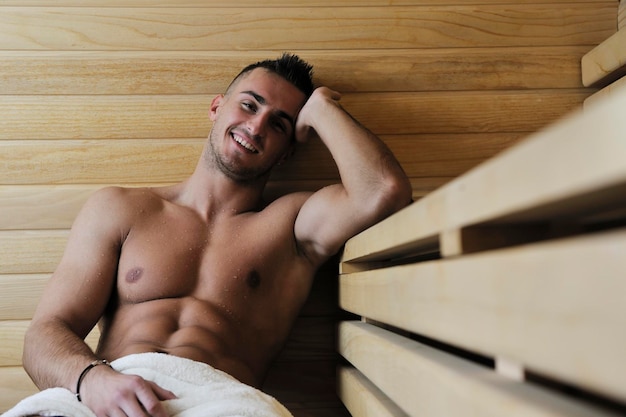 glücklicher, gut aussehender und attraktiver junger Mann mit muskulösem Körper, der sich in der heißen Sauna entspannt