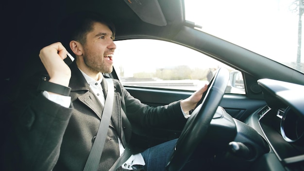 Glücklicher gutaussehender Geschäftsmann, der Auto fährt und singt Der Mensch ist glücklich, nachdem er Geschäfte gemacht hat und nach Hause fährt