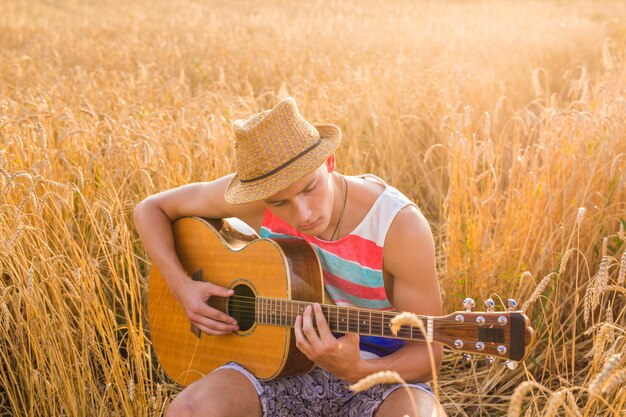 Glücklicher gutaussehender Mann spielt Gitarre auf dem Feld