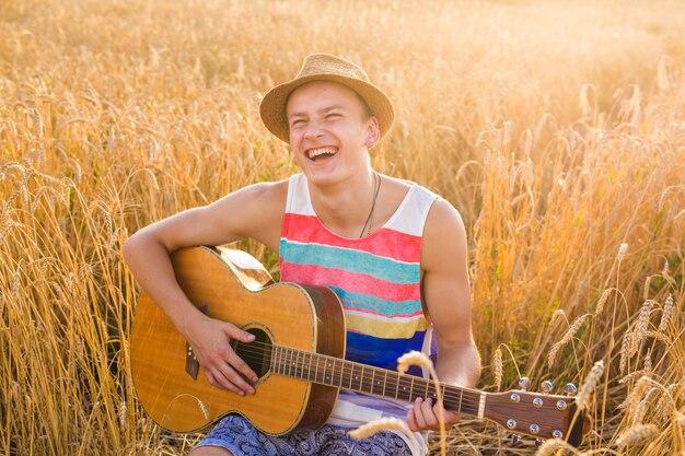Glücklicher gutaussehender Mann spielt Gitarre auf dem Feld