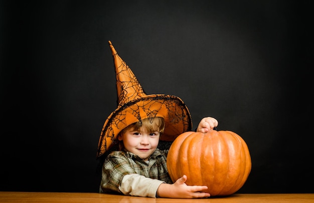 Glücklicher halloween-süßer junge im hexenhut mit halloween-kürbis-jack-o-laterne-trick oder halloween behandeln