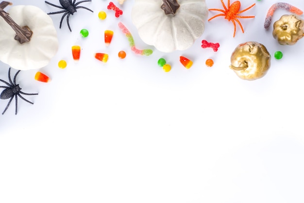 Glücklicher Halloween-Tagesfeiertagshintergrund. Flache Lage mit Süßigkeiten und Dekorationen für Kinderpartys, Eimerpackung mit Spinnen, Süßigkeiten, Fledermaus, auf weißem Tischkopierraum-Draufsichtsrahmen