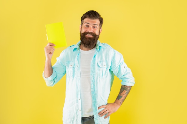 Glücklicher Hippie-Typ, der Notizbuch auf gelbem Hintergrundleser liest