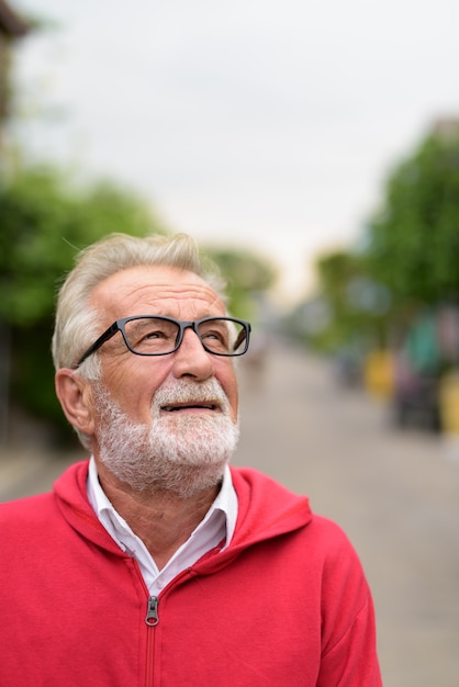 Glücklicher hübscher älterer bärtiger Mann, der lächelt, während er draußen mit Brillen denkt und schaut