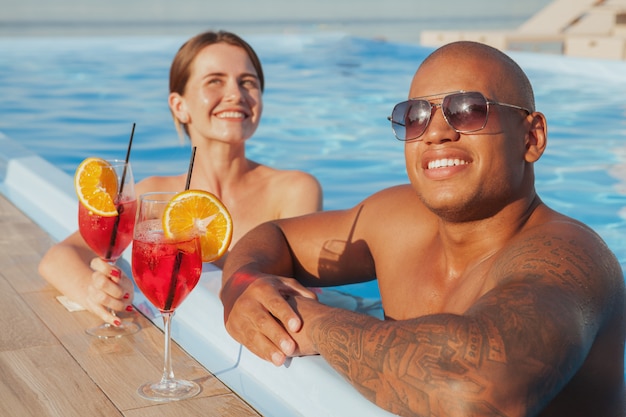Glücklicher hübscher afrikanischer Mann und seine Freundin, die im Schwimmbad entspannen und ihre Sommerferien genießen. Meer, Resort, Hotelkonzept