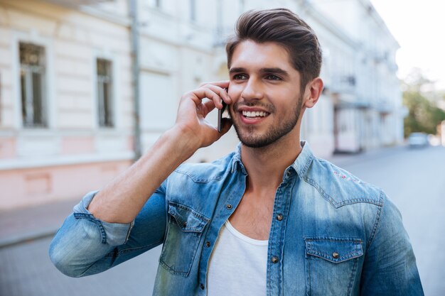 Glücklicher hübscher junger Mann, der draußen am Handy spricht