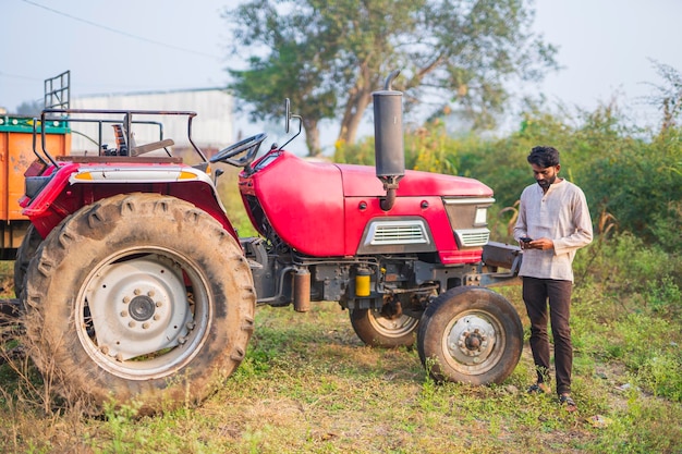 Glücklicher indischer Bauer mit Traktor auf landwirtschaftlichem Feld