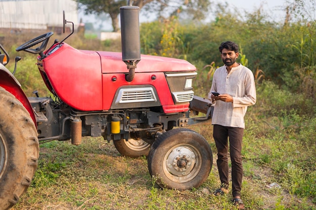 Glücklicher indischer Bauer mit Traktor auf landwirtschaftlichem Feld