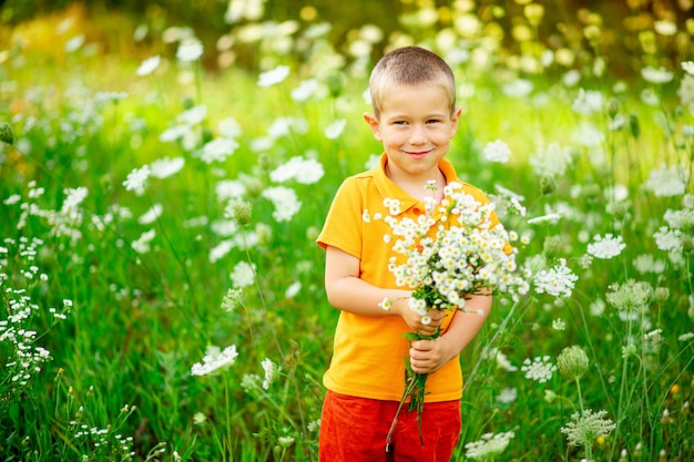 Glücklicher Junge auf dem Feld mit Blumen, die einen Blumenstrauß halten