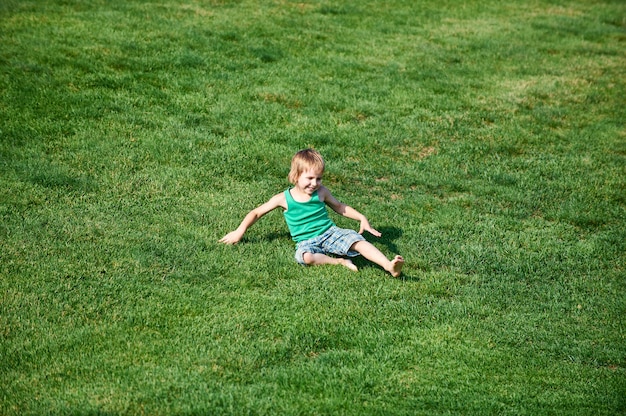 Glücklicher Junge, der am grünen Golfplatz am sonnigen Tag sitzt