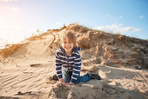 Glücklicher Junge, der am sonnigen Tag auf Sand springt