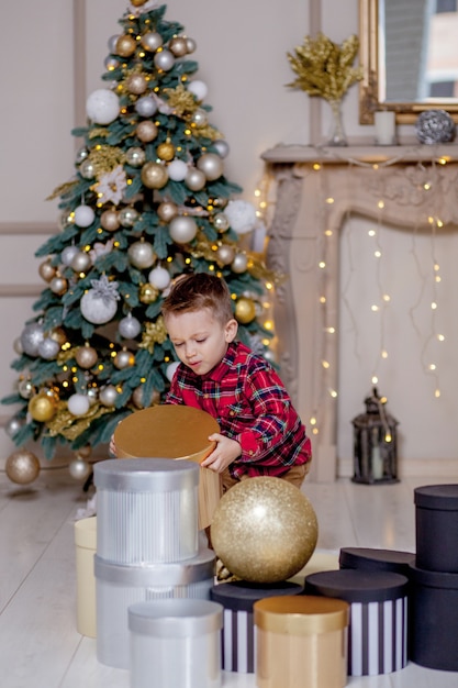 Glücklicher Junge, der auf Boden mit Weihnachtsgeschenken im dekorierten Raum liegt.