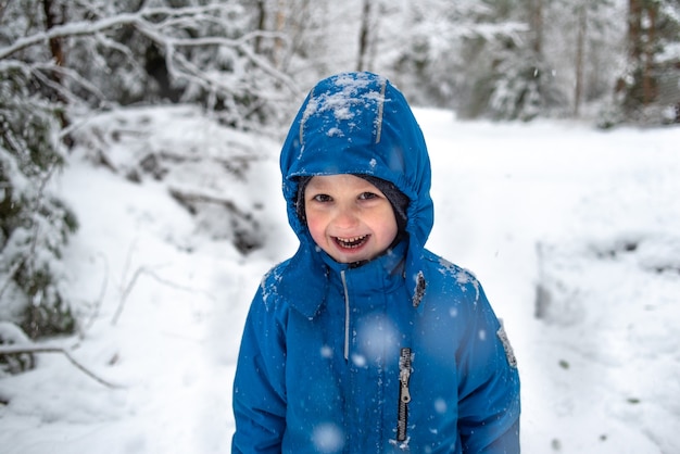 Foto glücklicher junge, der auf dem hintergrund des schneebedeckten winterwaldes lacht