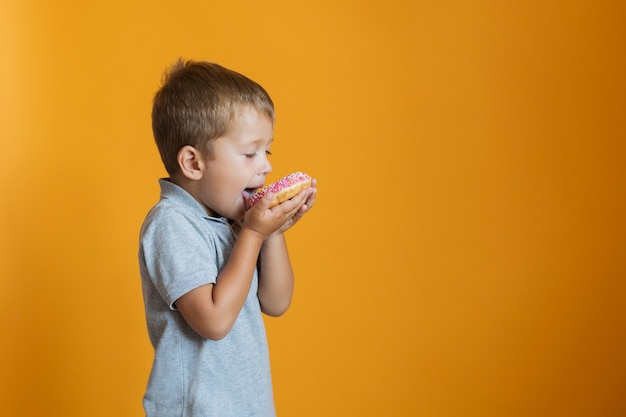 Glücklicher Junge, der Donut auf orange Wand isst