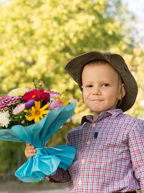 Glücklicher Junge, der einen großen Blumenstrauß in Geschenkverpackung als Geschenk für seine Mutter hält