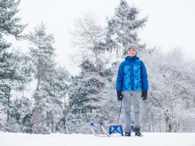 Glücklicher Junge fährt Schlitten und hat Spaß Kind spielt im Freien in Schnee Schlitten Kind Schlitten im schneebedeckten Park im Winter Außenspaß für die Kindheit Weihnachtsurlaub