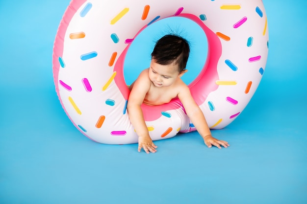 Glücklicher Junge im Badeanzug mit Schwimmringkrapfen auf einer farbigen blauen Wand