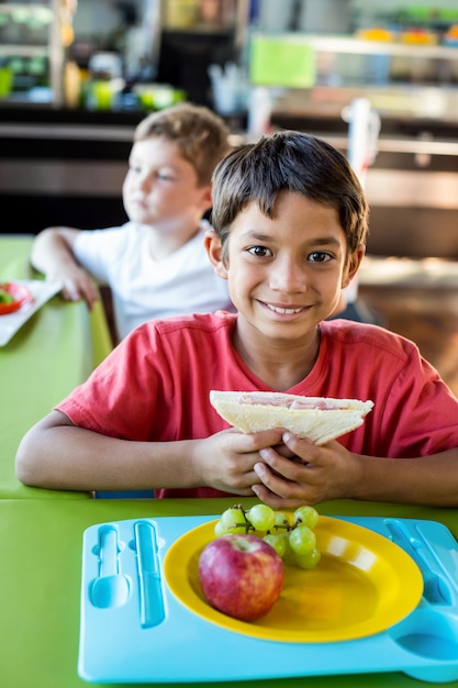 Glücklicher Junge mit Klassenkameraden, die Mahlzeit haben