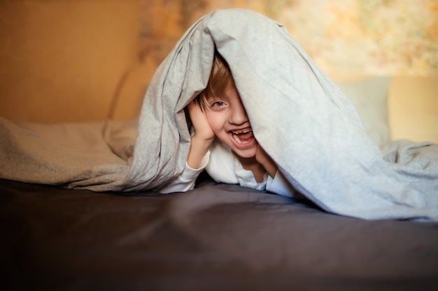 glücklicher Junge unter der Decke auf dem Bett